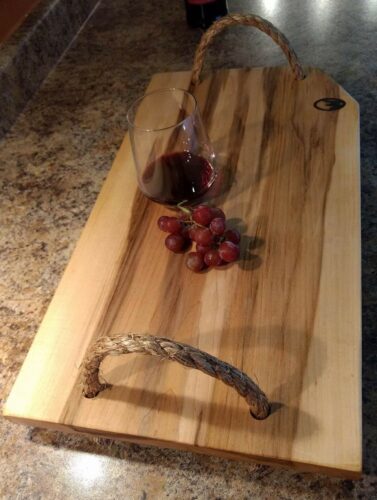 Une planche de bois avec des cordes comme poignées et un verre de vin et des raisins posés sur la planche