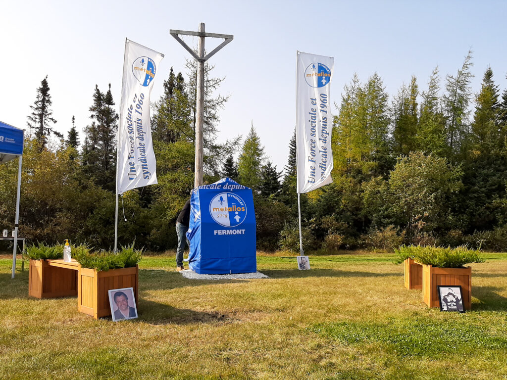 Le monument est couvert d'une toile bleue avec le logo des Métallos. Le monument est encadré de deux drapeau du Syndicat, ainsi que de deux bancs de bois, sur lesquels sont accotées des photographies de métallos décédés. 