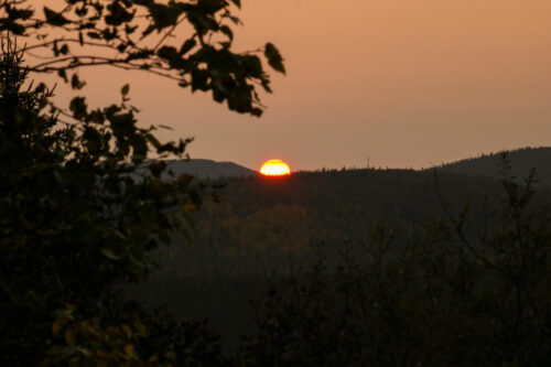 Soleil d'une couleur très orangée se couchant sur les montagnes autour de Fermont, avec des branches d'arbre en avant plan
