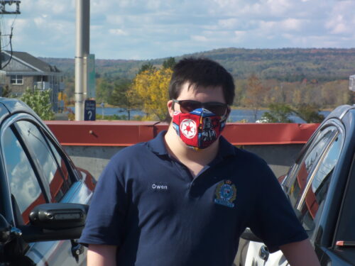 Le « Flic Owen » entre deux voitures portant un masque, des lunettes de soleil et son uniforme 