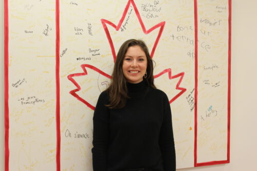 Célestine Mayhew souriante devant un drapeau canadien dessiné et signé par plusieurs