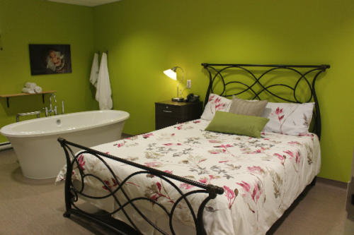 Dans une chambre aux mur vert se trouve un lit au couvre-lit fleuri. À Côté du lit il y a une biagnoire.