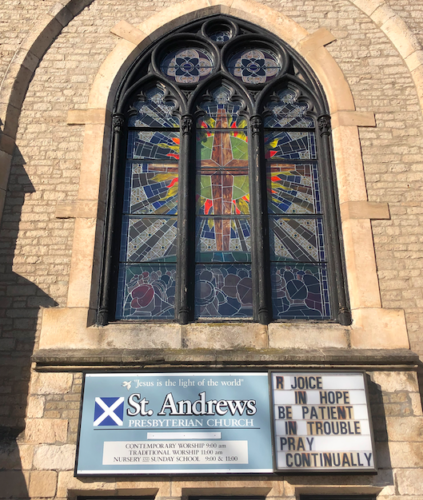 The exterior of St. Andrew's Presbyterian Chuch and its stained glass window above the main entrance sign.
