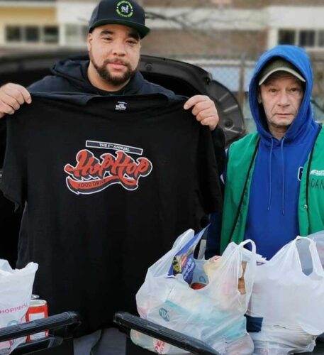 Justin Gunderson holds up a black hoodie for the Hip Hop Food Drive next to a volunteer.
