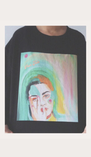 Peinture couleur pastelle du visage d'une femme sur un pull noir 