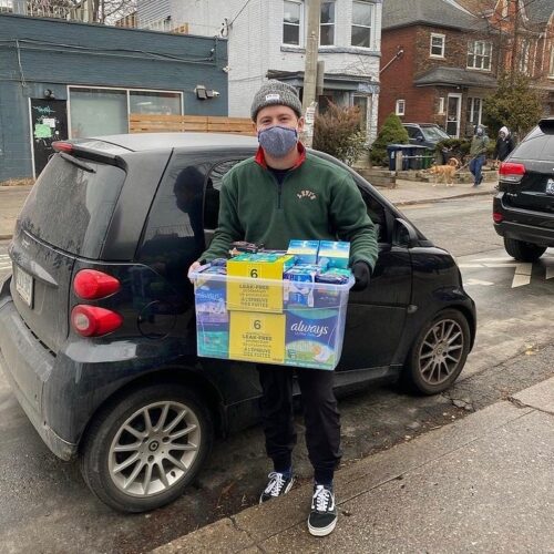 Will Hanlon holding a box of menstrual products in front of a car