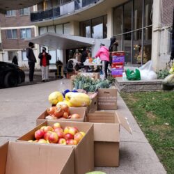 boxes of donation food lined up on sidewalk, leading up to apartment building.