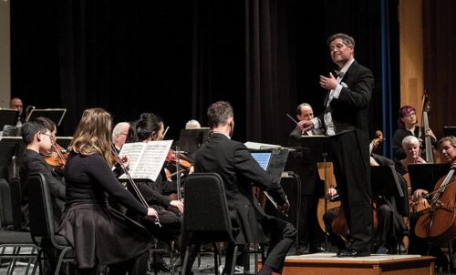 A conductor and orchestra in black tie attire ready to perform. 