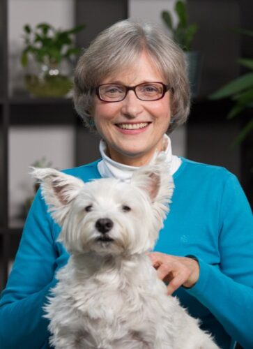 A professional shot of Liz White smiling and holding a white dog