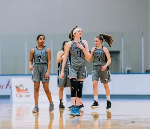 Four female Grade 10 basketball players wearing grey jersey are seen on a high school basketball court walking in the centre