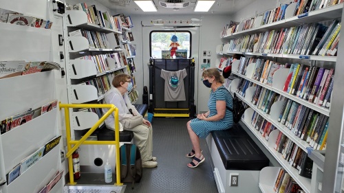 Two people sit on benches across from each other inside the bookmobile