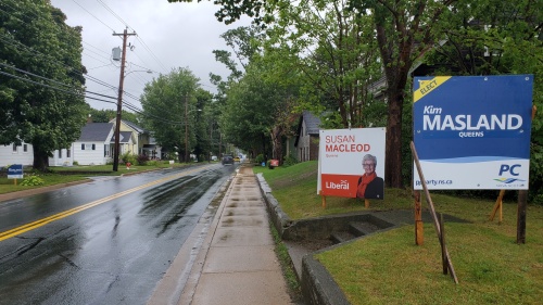 Election signs line both sides of a main street on a rainy day