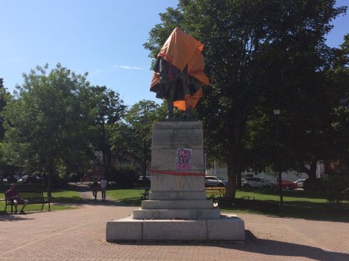 La statue de Cornwallis est recouverte d'une bâche orange. La statut est dans un parc et il y a une pancarte en dessous "Make it right" est écrit sur la pancarte.