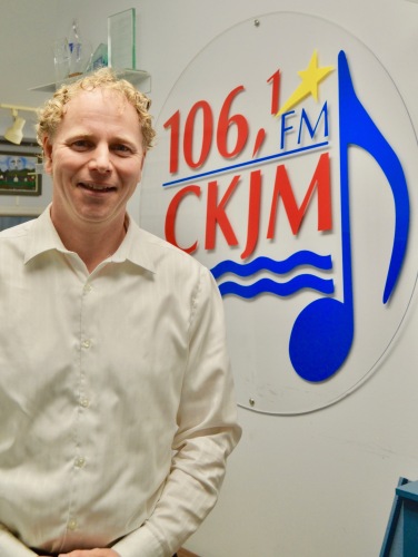 Homme politicien avec chemise blanche en avant du logo de Radio CKJM.