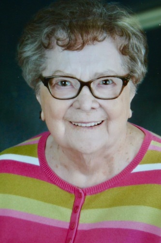 Dame âgée avec lunettes, portant un chandail rose, vert et blanc.