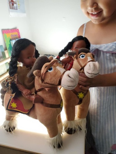 Young indigenous girl playing with two dolls riding on two horse.