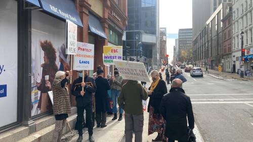 Du monde avec des pancarte assemble dans la rue, il y a de la circulation. C'est un centre ville