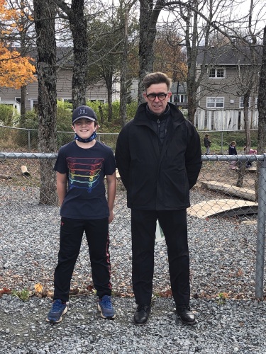 Un élève de 10 - 12 ans avec une casquette pose a coté de son enseignant, un homme d'une quarantaine d'années. Ils sont dehors dans un parc d'école.