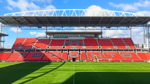 Red seats in an outdoor arena with a green soccer field.