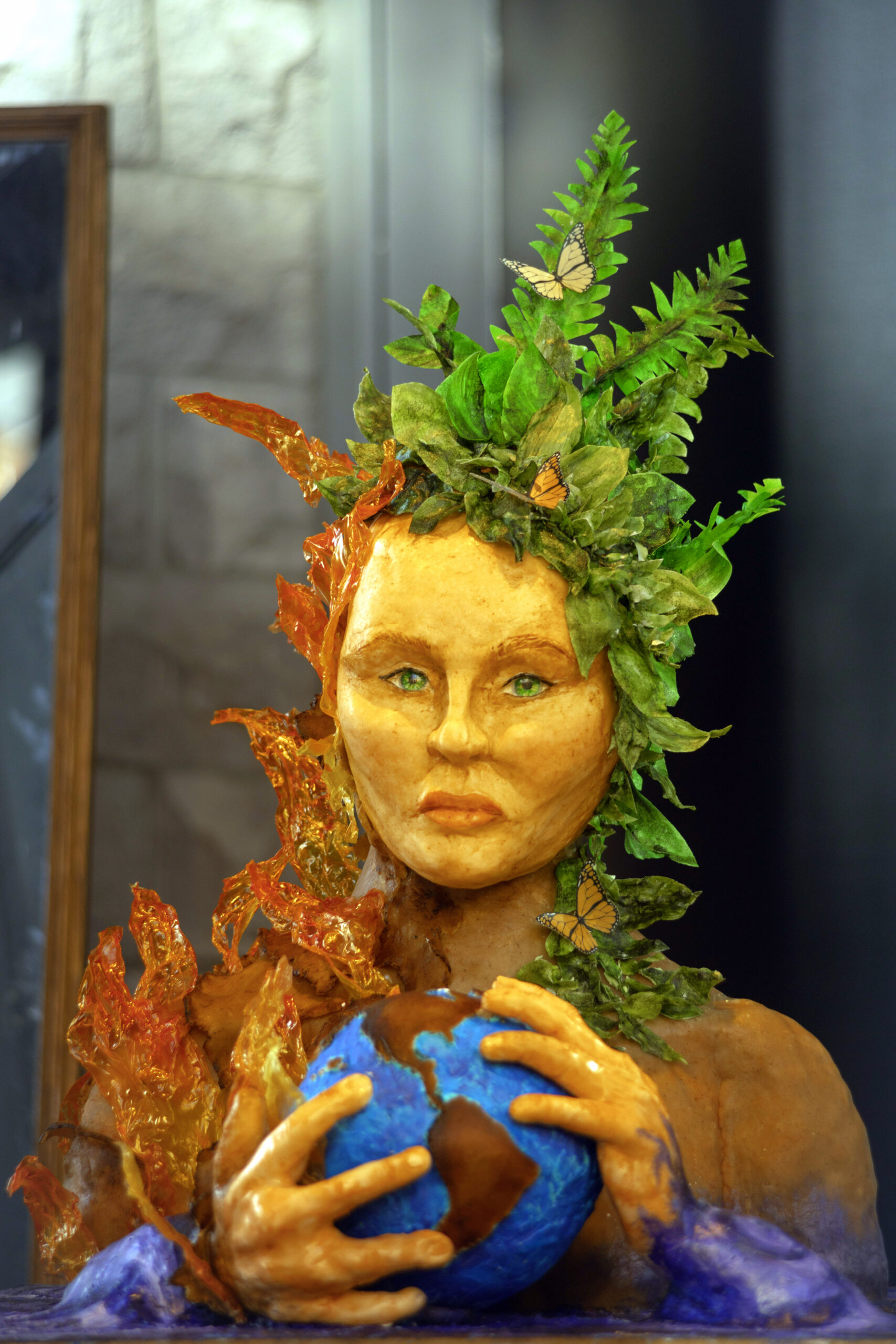 Femme tenant une balle ronde bleue avec le continent américain nord et sud dessiné et visible entre ses mains, sa chevelure est faite de feuilles vertes sur la droite et de feuilles d'automne sur la gauche