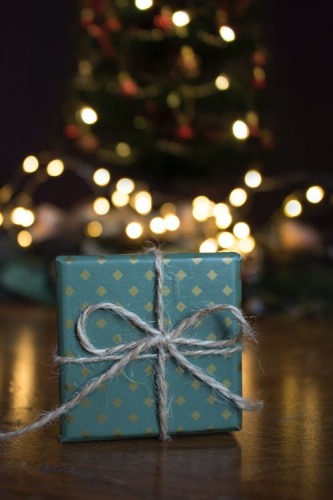 Cadeau de Noël emballé de papier bleu en avant d'un arbre de Noël allumé.