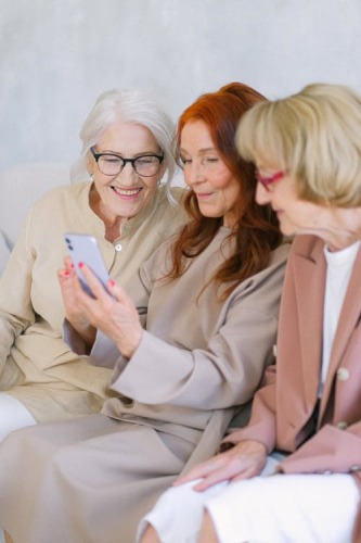 Trois dames âgées assises regardant un téléphone cellulaire.
