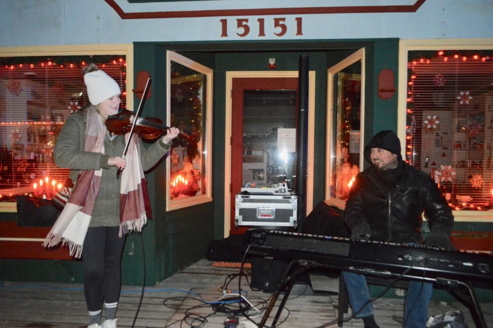 Une femme jouant du violon et un homme jouant du piano à l'extérieur d'un magasin en soirée.