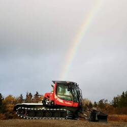 Une dameuse de sentiers de motoneige avec un arc-en-ciel en arrière plan.