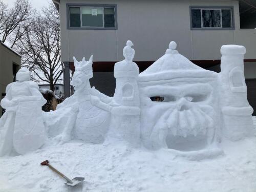 A snow sculpture depicting a castle, with a dragon and armoured knight standing next to it.
