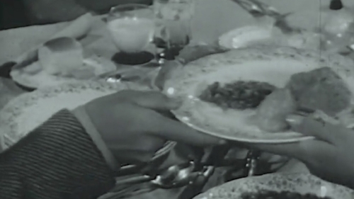 Black and white film reel showing someone handing a dinner plate with food on it to someone else's hand