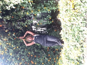 Jeune femme noire en salopette noire sous un oranger avec les bras au dessus de la tete et les paumes des mains jointes