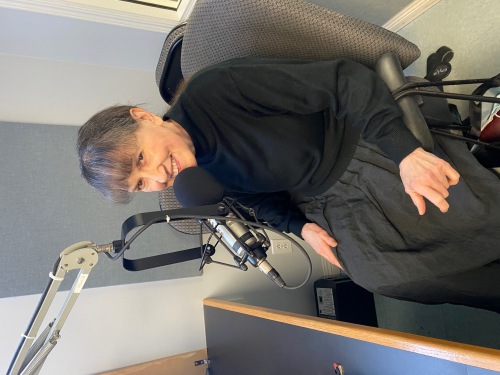 Dame habillée en noir assise à un micro dans un studio de radio.