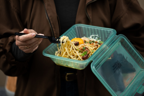 contenant en plastique ouvert avec des nouilles à l'intérieur et une personne qui prend la nourriture avec une fourchette en plastique