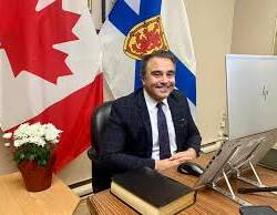 Homme assis à un bureau avec drapeaux du Canada et de la Nouvelle-Écosse en arrière plan.