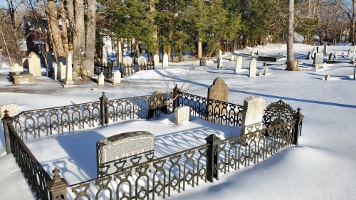 A cemetery covered in snow with a forest in the background. It is a sunny day. 