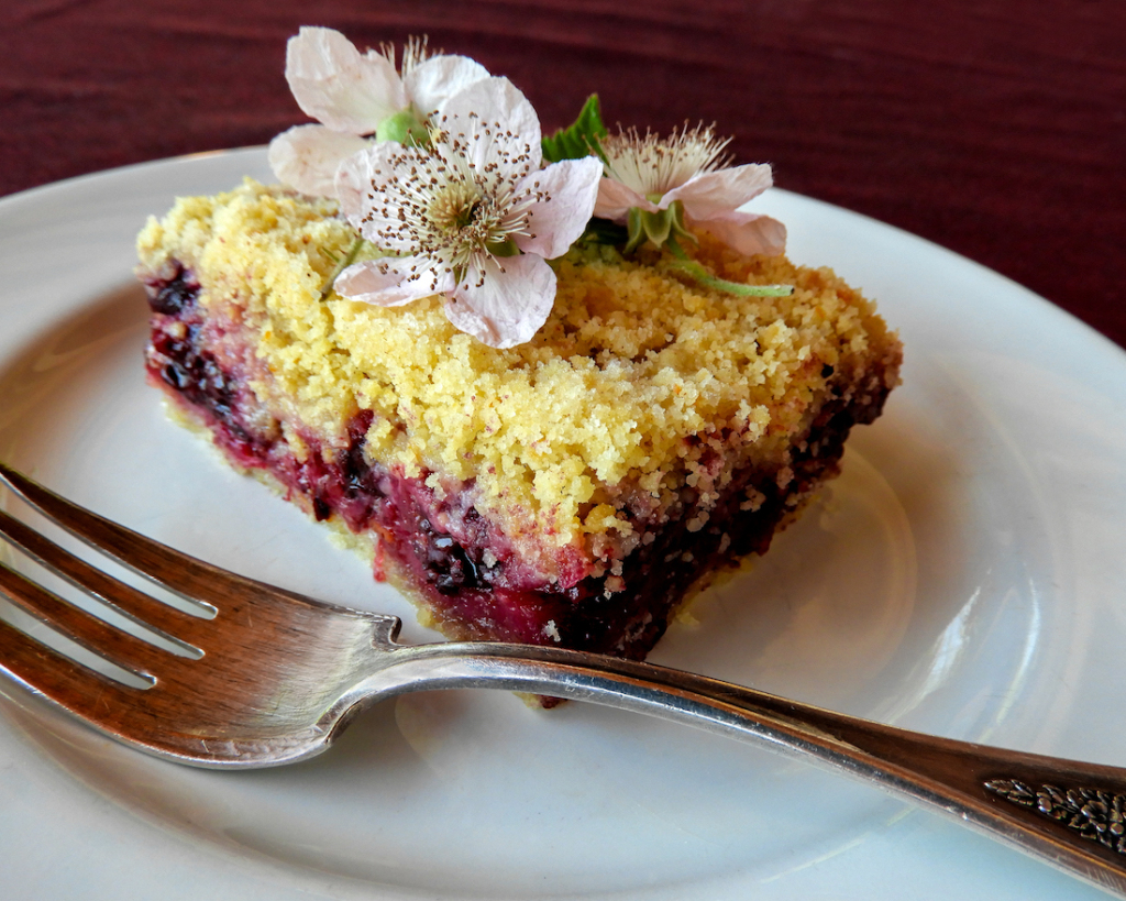 A dessert square with flowers decorating its top sits on a white plate alongside a fork.