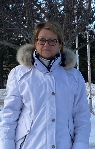 Une femme se trouvant à l'extérieur et portant un manteau d'hiver blanc sourit à la caméra.