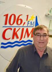 Homme avec lunettes et chemise noire en avant du logo de Radio CKJM.