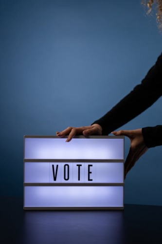 Des bras tenant une enseigne illuminée avec le mot VOTE.