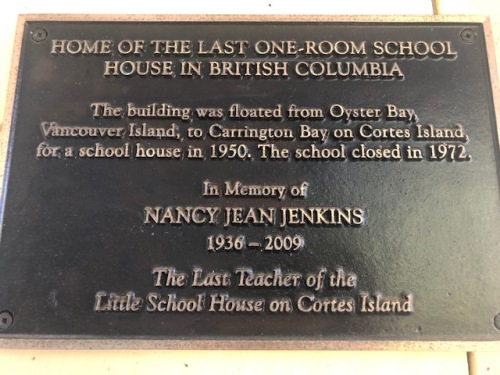 A metal plaque next to the Old Schoolhouse Gallery entrance describes how the structure came to be on Cortes Island.