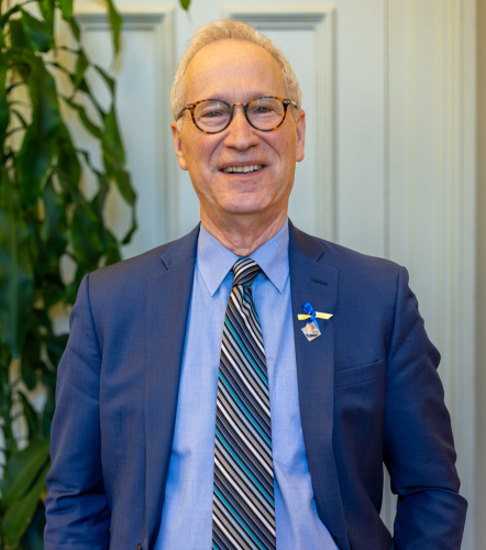 Un homme souriant aux cheveux blancs en veston et cravate bleus.