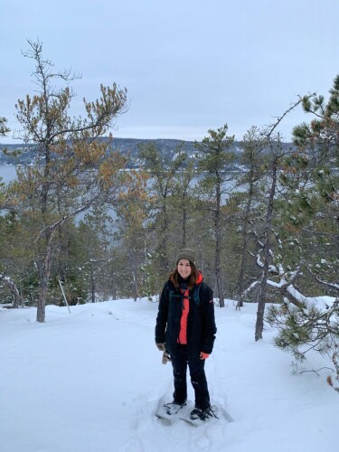 Femme à l'extérieur sur la neige avec des arbres autour d'elle.