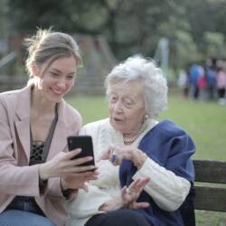 Une jeune dame et une dame âgée assise sur un banc regardant un téléphone intelligent.