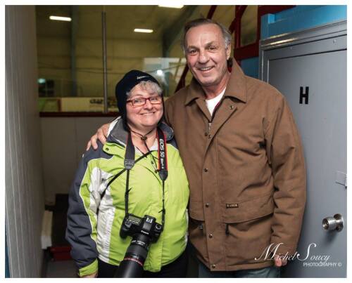 Une femme photographe portant un gilet vert accompagné de l'ancien joueur de hockey Guy Lafleur.