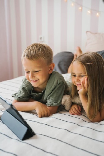 Deux enfants allongés sur fin lit examinant un écran.