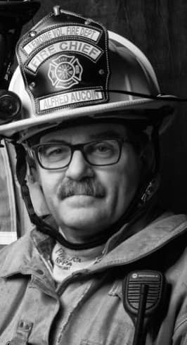 Un homme avec lunettes et moustache portant un habit de pompiers.