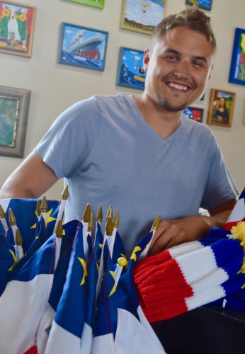 Un jeune homme portant un chandail bleu en arrière de drapeaux acadiens.