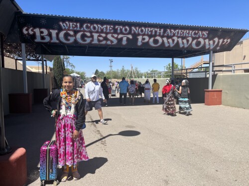 Image shows Demi Potts standing in front of sign that reads "Welcome to North Americas Biggest POWWOW!"