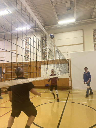 Une femme, deux hommes de chaque côté d'un filet attendent qu'un ballon de volley-ball descende.