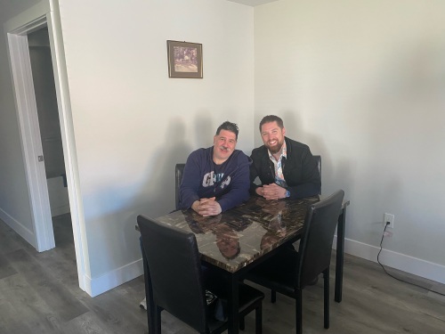 Michael Walsh is smiling and sitting with Craig Boutilier in a small dinner table at Boutilier's new apartment